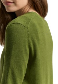 Jersey verde de punto con cuello redondo, textura suave y detalles sutiles de costura en el hombro. Silueta ajustada.