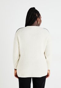 Κρεμ ζακέτα ριπ με χαλαρή εφαρμογή και μακριά μανίκια. Διαθέτει μαύρη ραφή κατά μήκος των ώμων. Απαλή υφή και elongating σχήμα.