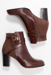 Bottes cheville en cuir marron avec un panneau en daim marron texturé, ornées d'une boucle dorée et d'une fermeture éclair latérale, sur un talon noir épais.