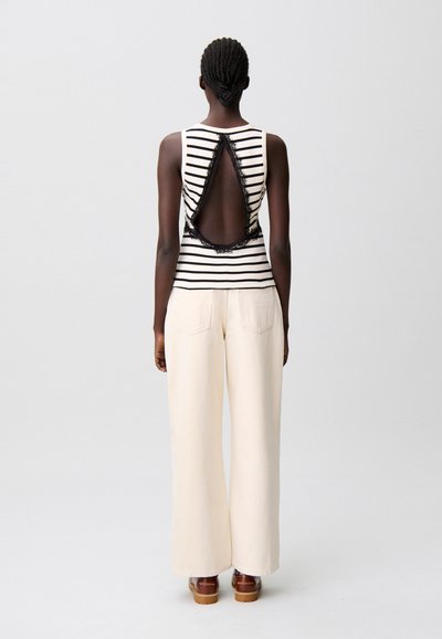 Top senza maniche a righe con schiena scoperta impreziosita da pizzo, abbinato a pantaloni a gamba larga a vita alta color crema e scarpe con plateau in legno.