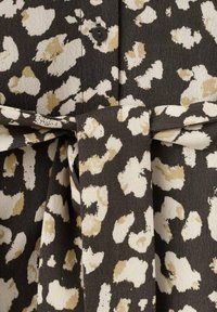 Zwarte stof met beige en witte luipaardprint; met een knoopdetail en een ceintuur die gestrikt kan worden. Gladde textuur.