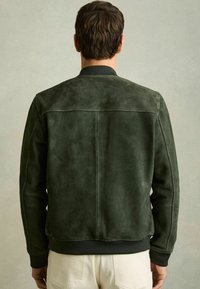 Jachetă bomber din suede verde închis, cu guler ribbit, manșete adaptate și o textură netedă, având un design curat și minimalist.