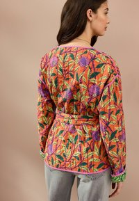 Veste à motif floral multicolore en orange, vert et violet avec ceinture enveloppante, manches longues et bordure contrastante aux poignets et à l'encolure.