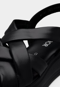 Μαύρο δερμάτινο σανδάλι με πλεγμένους ιμάντες, αναπαυτική εσωτερική σόλα και ελαφρύ τακούνι τύπου πλατφόρμας. Λείο υφή και μινιμαλιστικές λεπτομέρειες σχεδίασης.