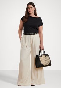 Haut noir à épaules dénudées, pantalon large crème, ceinture noire et un sac à main structuré noir avec des détails en tressé. Boucles d'oreilles simples.