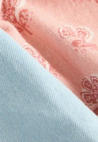 Deux morceaux de tissu : l'un est rose pastel avec un motif floral et l'autre est bleu clair. Les textures sont lisses et tissées, avec des fibres visibles.