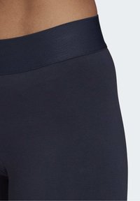 Gros plan sur une personne portant des leggings taille haute bleu marine foncé avec une large ceinture élastique, sur un fond clair.