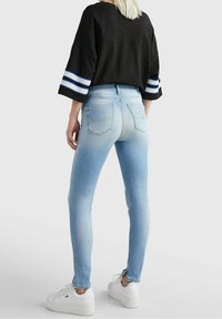 Jeans ajustados de cintura alta en un tono azul claro con una textura de denim suave, cinco bolsillos y costuras visibles, combinados con una blusa negra y zapatillas blancas.