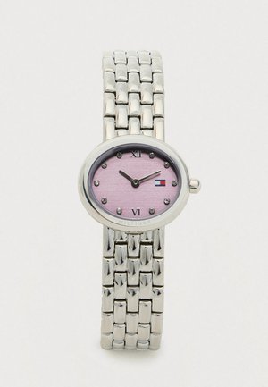 Zilveren metalen schakelhorloge met een ovale roze wijzerplaat, kristallen uurmarkeringen, Romeinse cijfers op 12 en 6, en het Tommy Hilfiger-logo nabij 3 uur.
