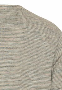 Nærbillede af en lyst beige og gråt fint stribet strikket stof, der viser skulder- og ærmeområdet.