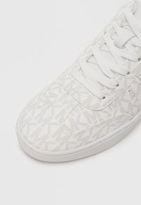 Baskets blanches avec un motif texturé et un bout rond. Lacets blancs, avec une languette rembourrée. Semelle en caoutchouc légèrement surélevée.