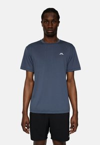 Mans kortärmad träningsskjorta i mörkblått tyg, med rund halsringning och en liten vit logotyp på bröstet.