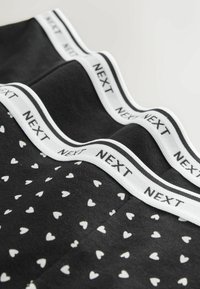 Czarna bielizna z białym wzorem serc oraz białym paskiem z napisem "NEXT" w prostym, nowoczesnym stylu.
