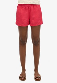 Shorts rossi in lino con vita elasticizzata, caratterizzati da una vestibilità rilassata e orli arrotolati. Abbinati a sandali a scivolo marroni.