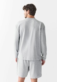 Gray long-sleeve sweatshirt with a relaxed fit, ribbed neckline, and matching gray shorts. Soft fabric with subtle texture, featuring a back pocket.