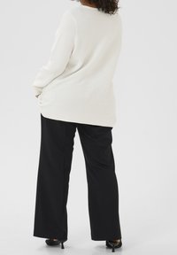Top de manga larga de canalé crema, combinado con pantalones de pierna ancha negros y tacones negros. El top tiene un corte holgado y un escote redondeado.