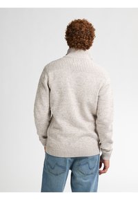 Harmaa neulottu villapaita, jossa on korkea ribbikraavu ja teksturoitu kuvio. Yhdistetty sinisiin farkkushortseihin, joissa on näyttävät takataskut.