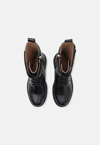 Botas de cuero negro con un acabado suave, que presentan un diseño de cordones, detalles en metal dorado y un forro interior marrón.