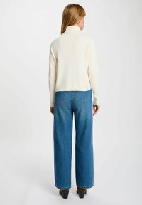 Pullover a collo alto a coste crema abbinato a jeans in denim blu a gamba larga e vita alta, con tasche posteriori e orlo pulito.