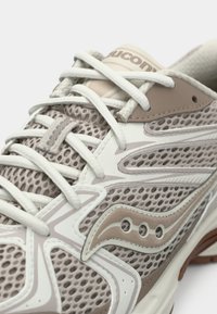 Lightweight running shoe featuring a mesh upper in beige and white, with contrasting accents, decorative stitching, and round laces.