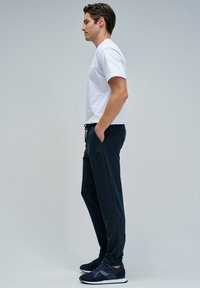 Joggers azul marino con bolsillos laterales, cintura con cordón y un parche. Combinados con una camiseta de manga corta blanca y zapatillas atléticas negras.