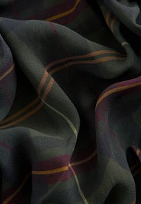 Tissu sombre à texture douce présentant un motif à carreaux composé de fines rayures orange, vertes et violettes sur un fond noir, délicatement plié.