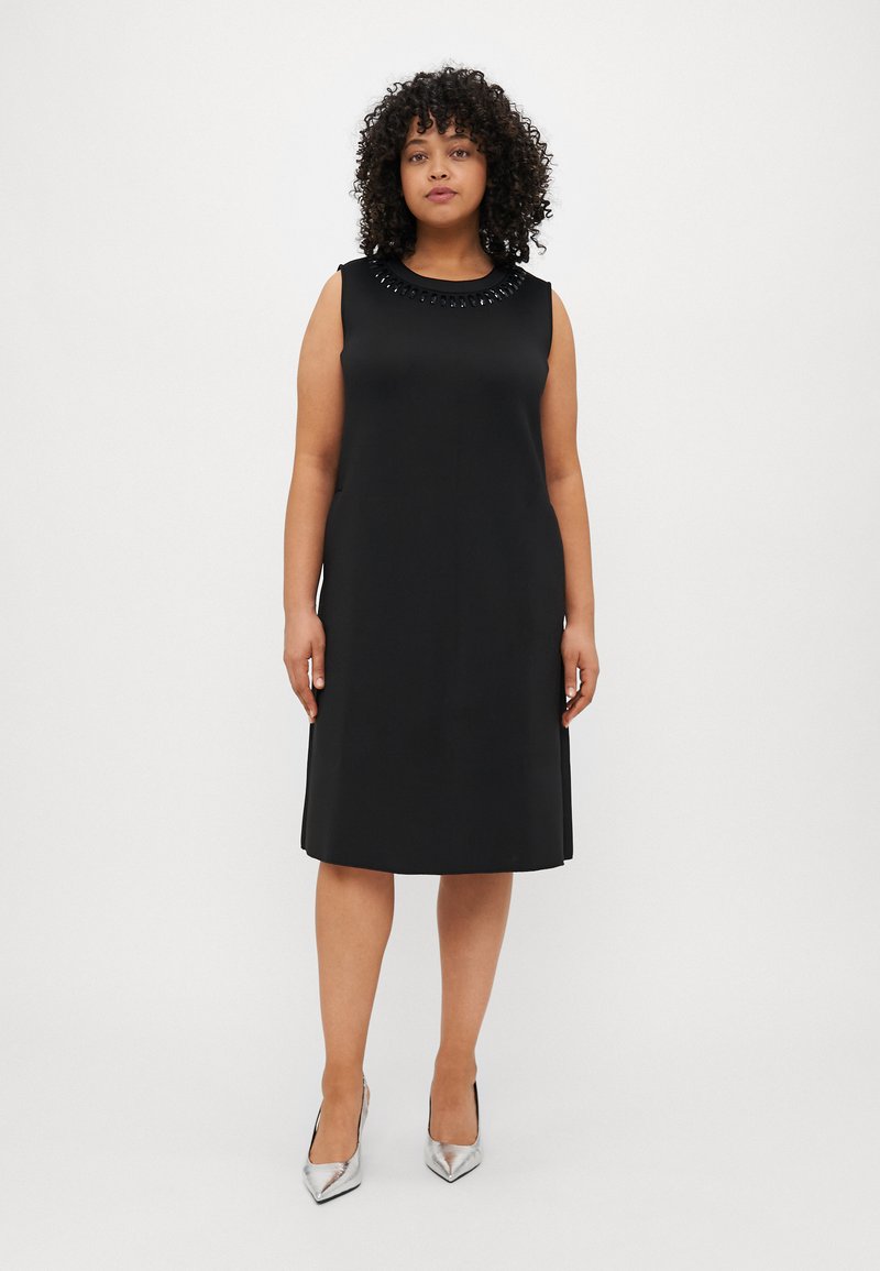 Μαύρο αμάνικο φόρεμα με στρογγυλή λαιμόκοψη και διακοσμητικές χάντρες. Λείος ύφασμα, σιλουέτα Α-γραμμής, έως το γόνατο, συνδυασμένο με ασημένια τακούνια.