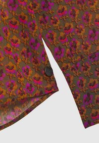 Gennemsigtig, mønstret stof med lilla og orange blomsterdesign på en brun baggrund. Inkluderer et sort, cirkulært mærke.