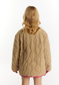 Vatteret beige jakke med bølget mønster, lange ærmer og en lys pink kant ved kanten. Blød tekstur og oversized pasform.