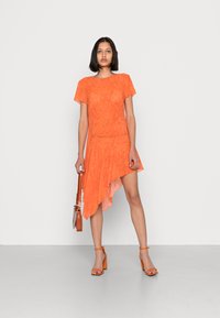 Vestido assimétrico laranja com mangas curtas, tecido texturizado e bainha fluida. Combinado com uma mala castanha e sandálias de salto laranja.
