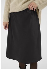 Jupe noire en satin de coupe A avec une taille élastique et une texture lisse, associée à un pull en maille beige, créant un look superposé.