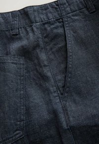 Primer plano de pantalones vaqueros azul oscuro que muestran cintura elástica, bolsillo delantero y costuras detalladas.