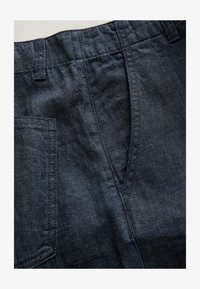Primer plano de pantalones vaqueros azul oscuro que muestran cintura elástica, bolsillo delantero y costuras detalladas.