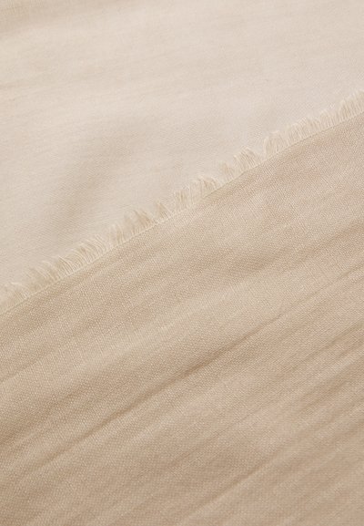Beige stoff med en myk, teksturert overflate. Har en frynset kant som går fra en lysere til en mørkere nyanse av beige.