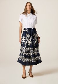 Cămașă albă cu mânecă scurtă, cu detalii cu butoni, combinată cu o fustă maxi bleumarin, cu modele florale albe și talie strânsă.