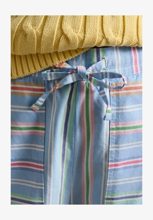 Strik gul sweater over blå stofshorts med vertikale og horisontale pastelfarvede striber, bundet med en sløjfe ved taljen.