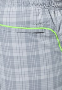 Gray plaid shorts with elastic waistband and neon green stitching along the pocket. Material appears lightweight and smooth.