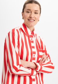 Red and white striped button-up shirt with long sleeves, featuring a collar and single chest pocket, made from a lightweight fabric.