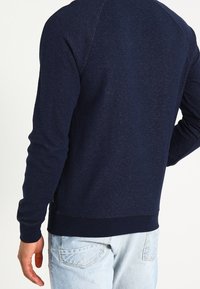 Sudadera azul marino de manga larga, con dobladillo y puños acanalados, de tejido texturizado. Presenta un cuello redondo y detalles de costura en contraste.