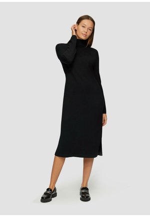 Zwart lange mouwen jurk met een hoge hals, voorzien van een rechte snit en een zijsplit. Draagend met zwarte instappers, gladde textuur en minimalistisch ontwerp.