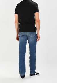 T-shirt nero a maniche corte abbinato a jeans dritti blu chiaro. I jeans presentano tasche posteriori e una leggera sfumatura, completati da sneakers nere.