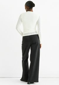 White, textured long-sleeve top with a fitted design, paired with high-waisted black wide-leg jeans. Both feature visible stitching details.