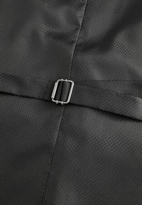 Schwarzer strukturierter Stoff mit einem hexagonalen Muster, das eine in das Design eines Gürtels integrierte silberne Metallgürtelschnalle aufweist. Glatte Oberfläche.