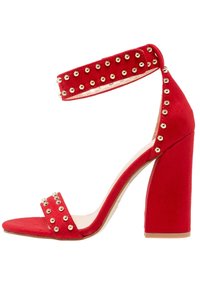 Sandalias de tacón alto de ante rojo con un grueso tacón en bloque, una correa en el tobillo con tachuelas y un diseño minimalista de punta abierta.