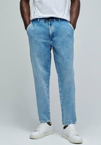 Pantalones de mezclilla azul claro con un corte relajado, que cuentan con bolsillos frontales y una cintura elástica con cordón, combinados con zapatillas blancas.
