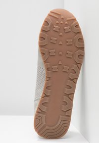 Semelle d'une chaussure gris clair avec une semelle extérieure en caoutchouc couleur tan présentant des motifs géométriques et des détails latéraux perforés.