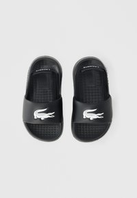 Μαύρα σανδάλια slide από λεία συνθετική ύλη, με λευκό λογότυπο κροκοδείλου και υφασμένες μαύρες εσωτερικές σόλες για καλύτερη πρόσφυση.