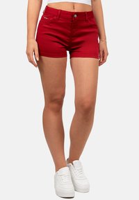 Shorts in denim rosso con design aderente, stile a cinque tasche e chiusura con bottone frontale, abbinati a sneakers bianche.