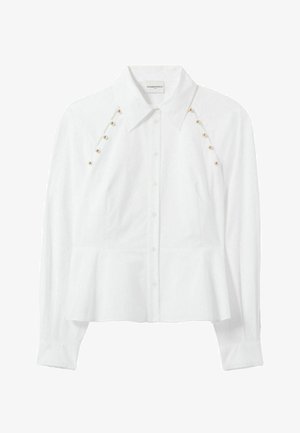 Blouse blanche à manches longues avec une taille ajustée et des boutons dorés décoratifs sur les épaules, offrant une apparence élégante.