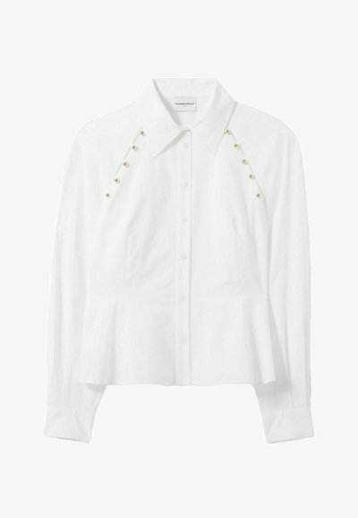 Blusa bianca a maniche lunghe con vita aderente e bottoni decorativi dorati sulle spalle, che trasmette un aspetto elegante.